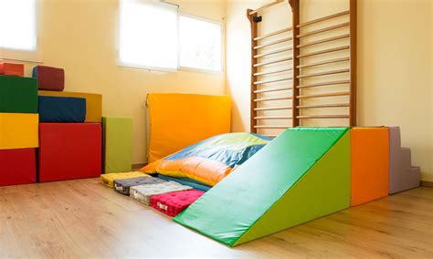 Interno di una stanza per psicomotricità con materassi colorati, blocchi morbidi e un percorso ad ostacoli